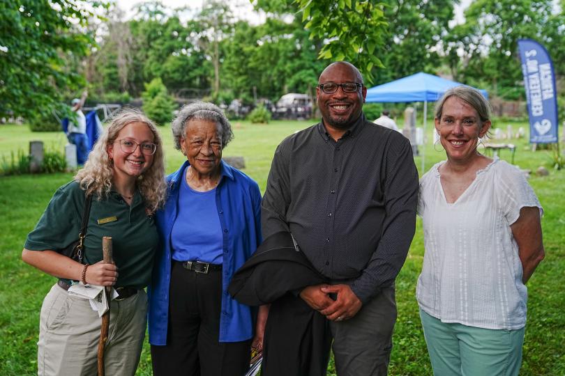 Four individuals stand close together outdoors, looking at the camera.
