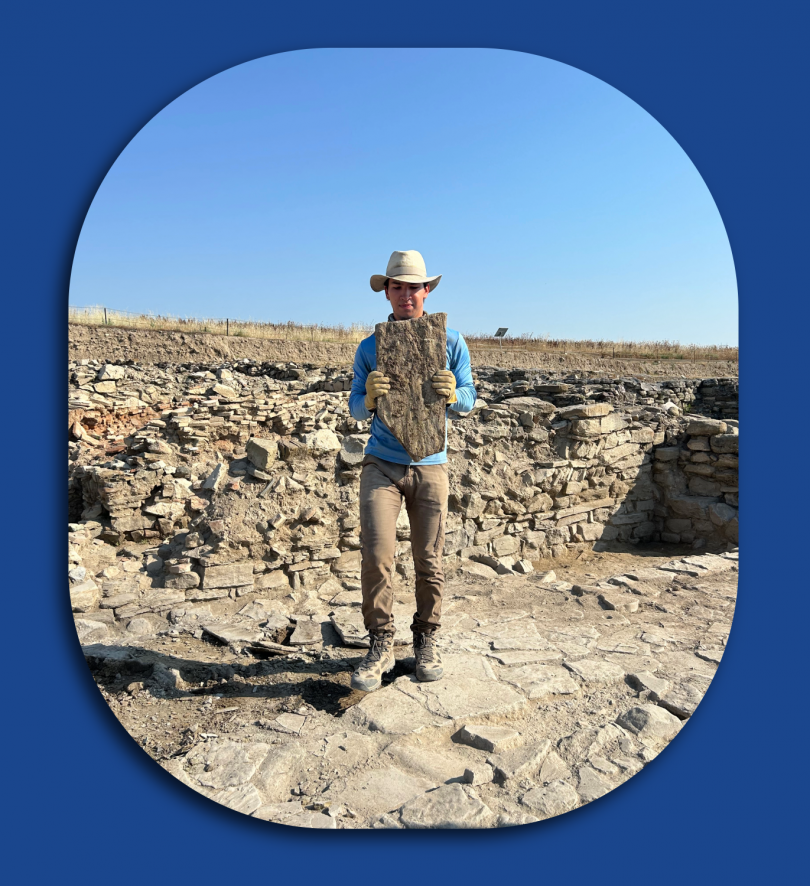 Man in work clothes stands with an artifact at a dig site.